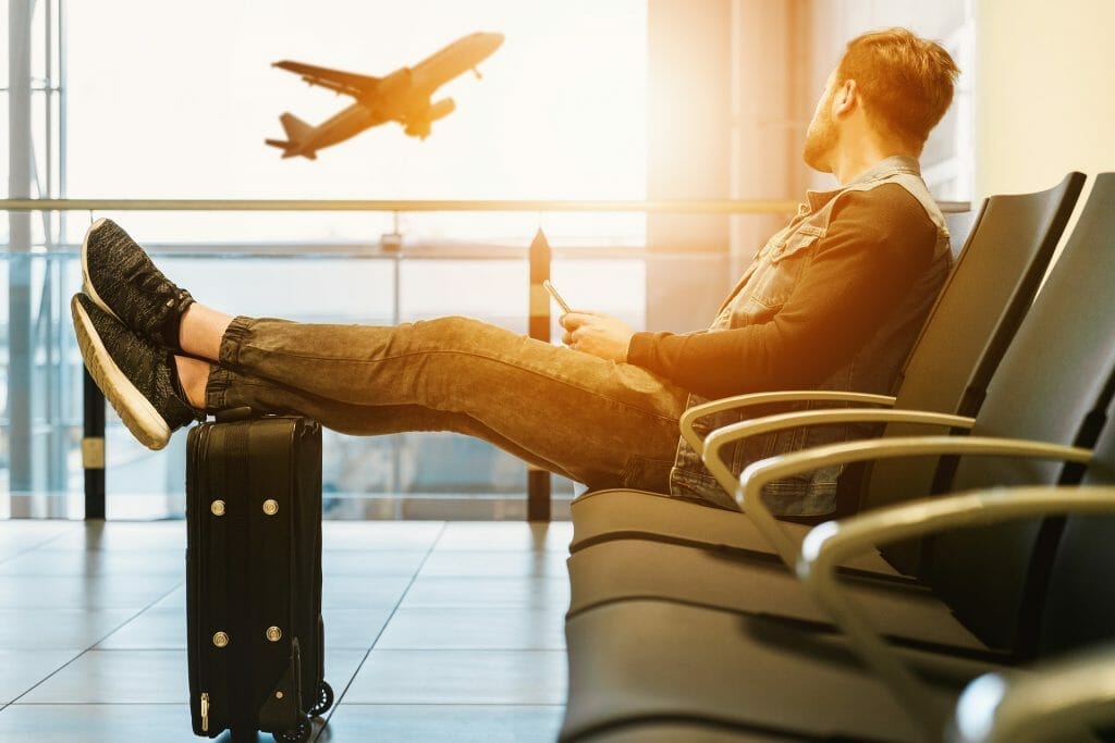 Nervous flyer man in airport with feet on bag looking at plane taking off