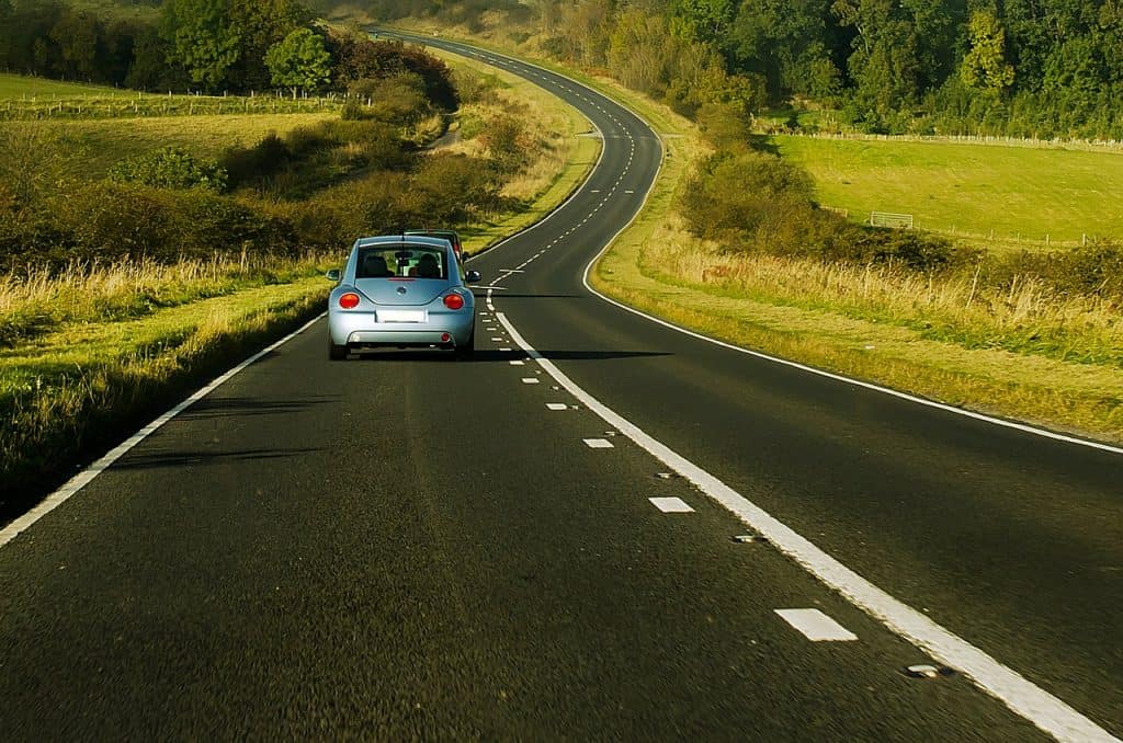 A car driving along a windy road with fields either side