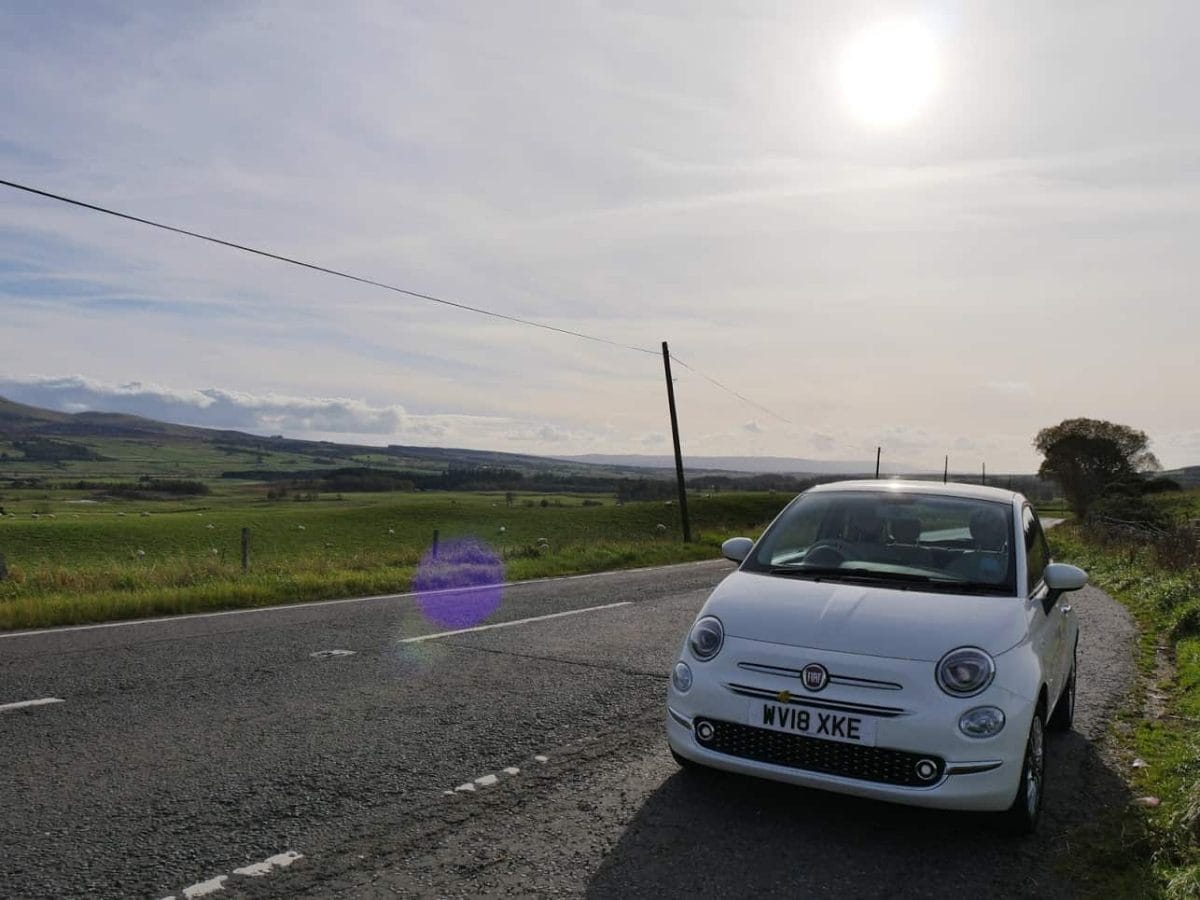A white car in Scotland with fields and the sun behind