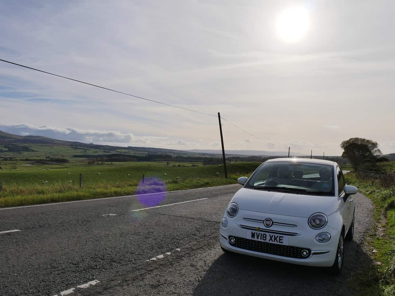 A white car in Scotland with fields and the sun behind
