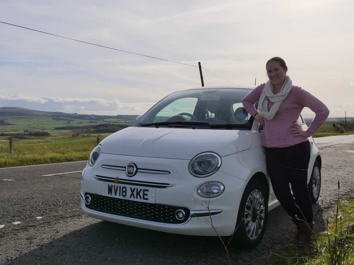 Kalyn leaning on a white car with green fields behind