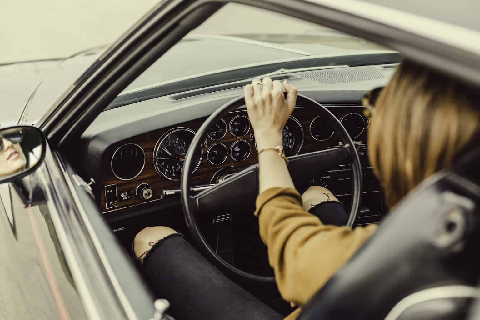 A lady seen from outside the drivers window driving a car