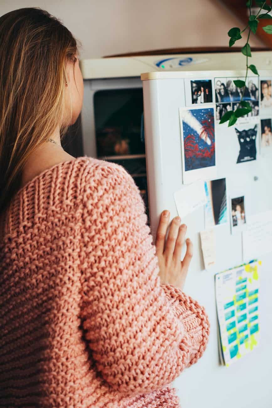 Girl in peach knitted sweater opening a fridge