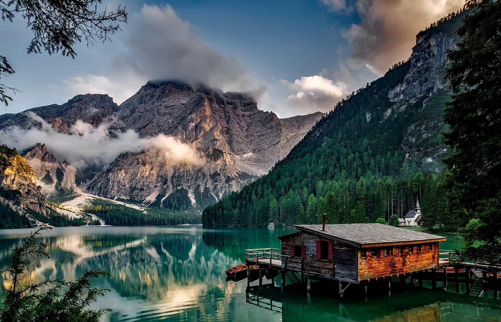 A highly-reflective lake with mountains in the background and a wooden shack over it