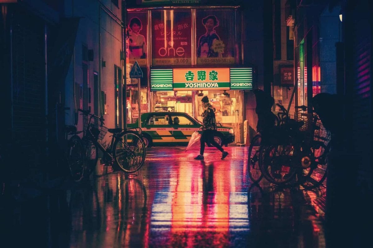 Japan at night with red lights reflecting on road and lady walking past with bikes on either side