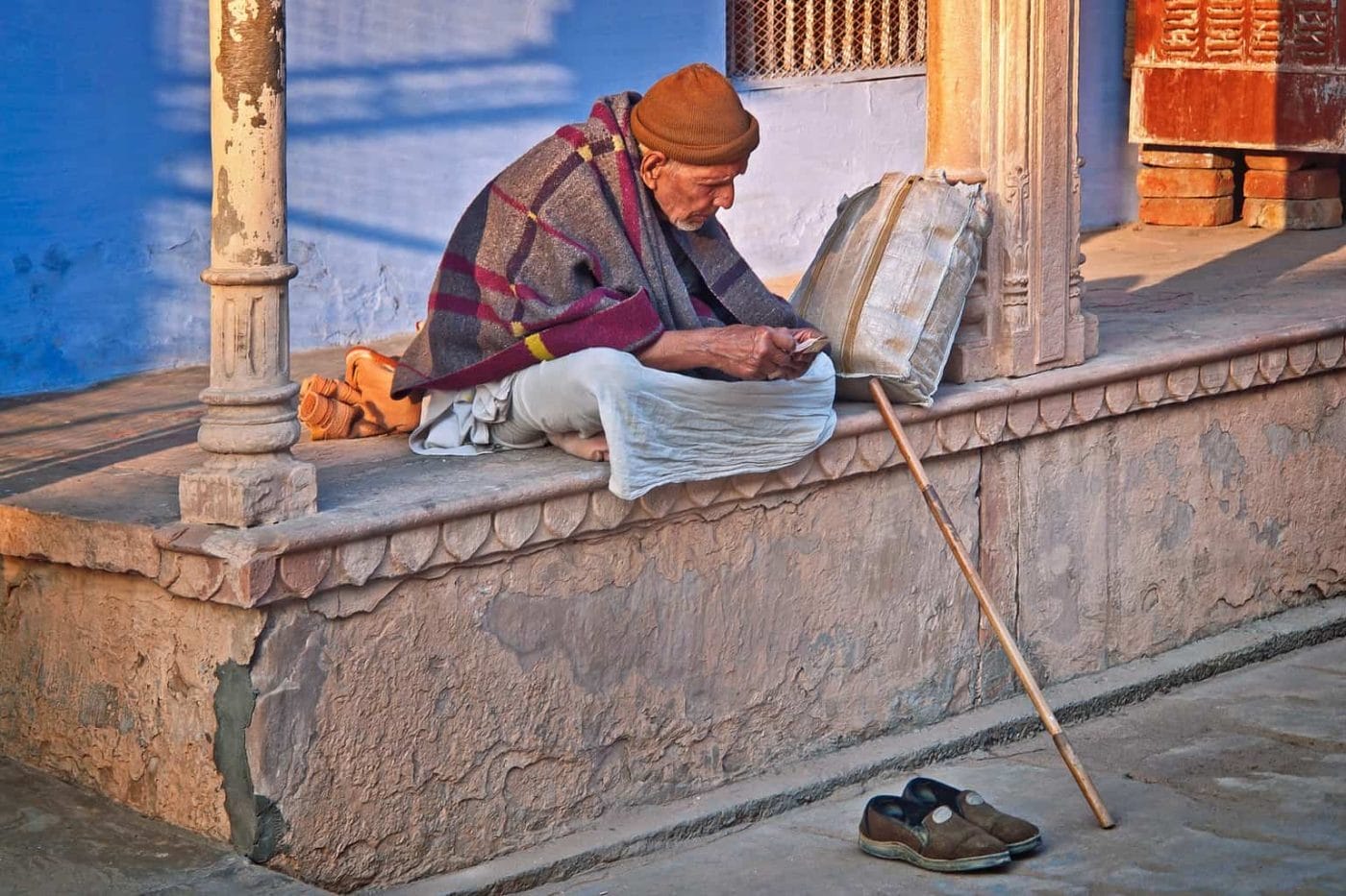 An old man sitting on a wall with a cane and shoes on the ground