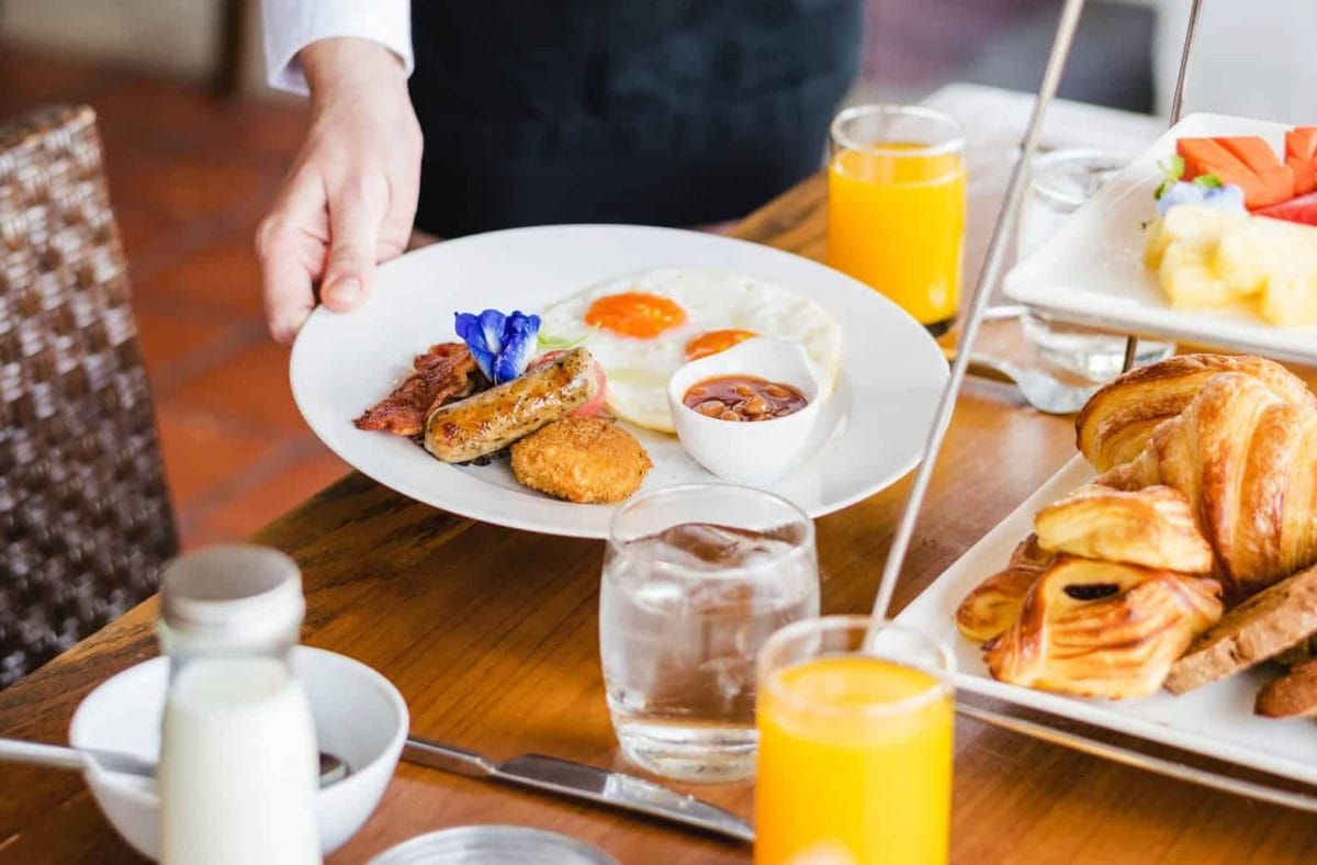 person holding plate of breakfast with baked beans eggs sausage hash brown and bacon