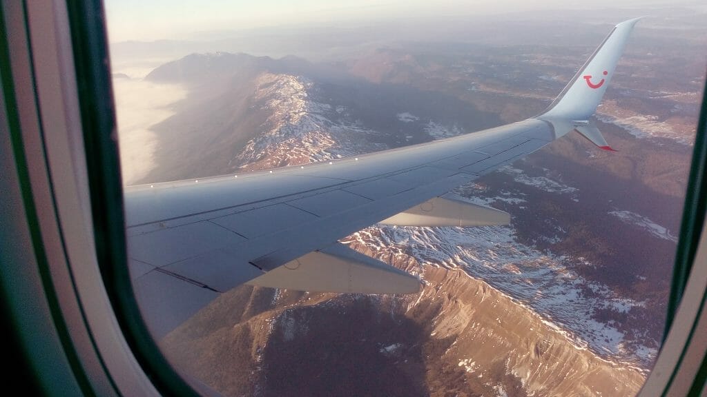 Airplane wing over snowy mountains seen out of window