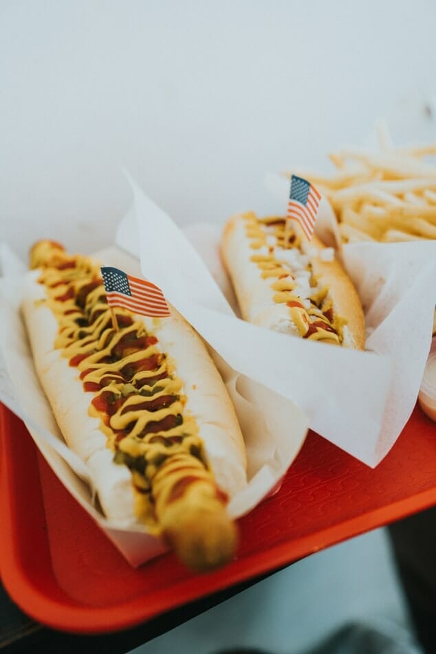 Hot dogs on a red tray with mustard and small USA flags sticking out of them