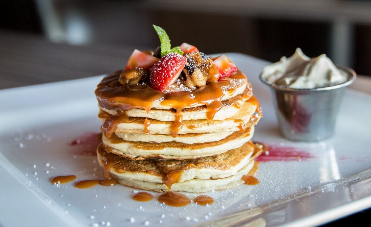 A stack of pancakes with strawberries on top and syrup dripping down the sides