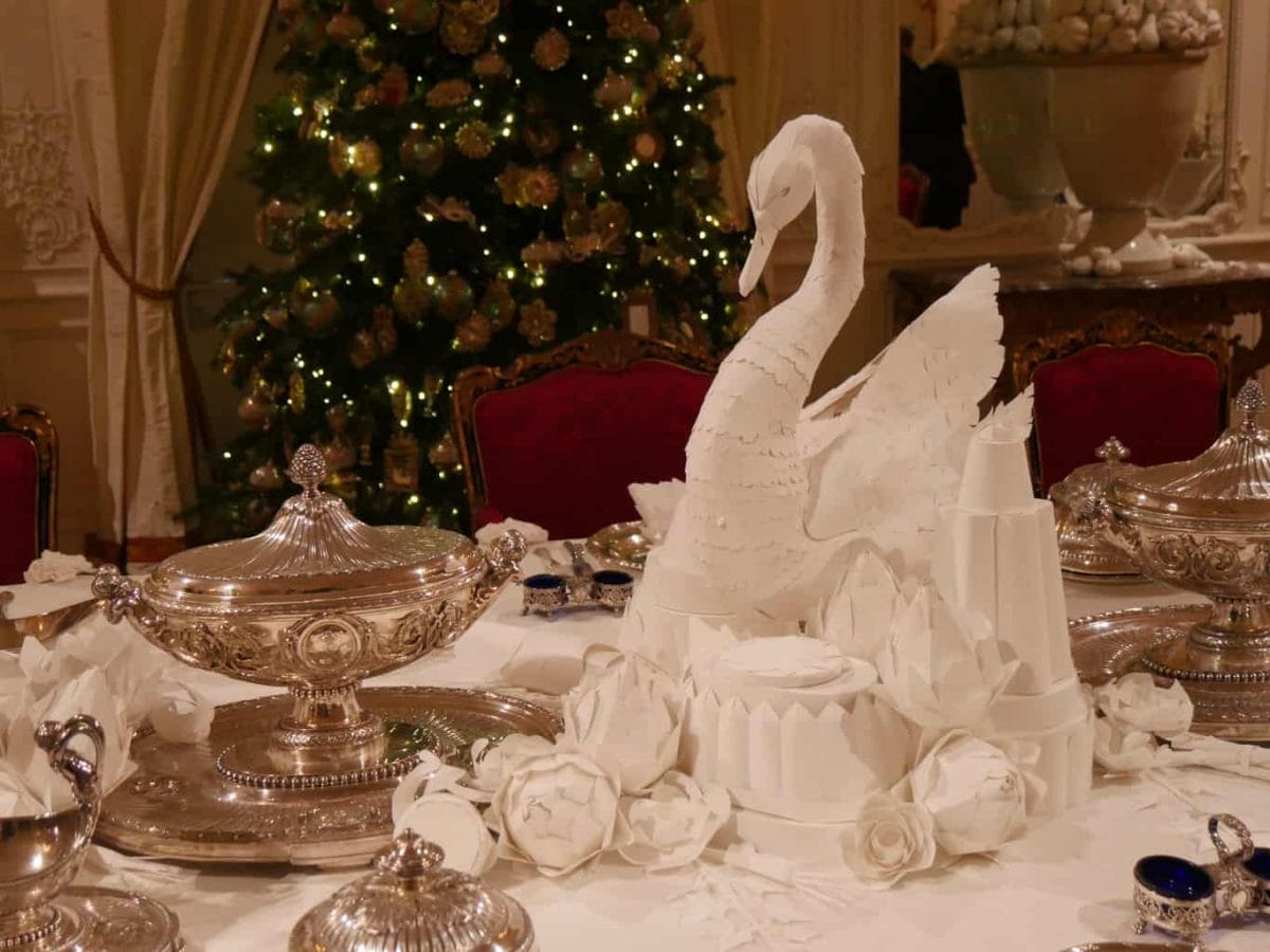 A paper swan on a table with a Christmas tree behind it