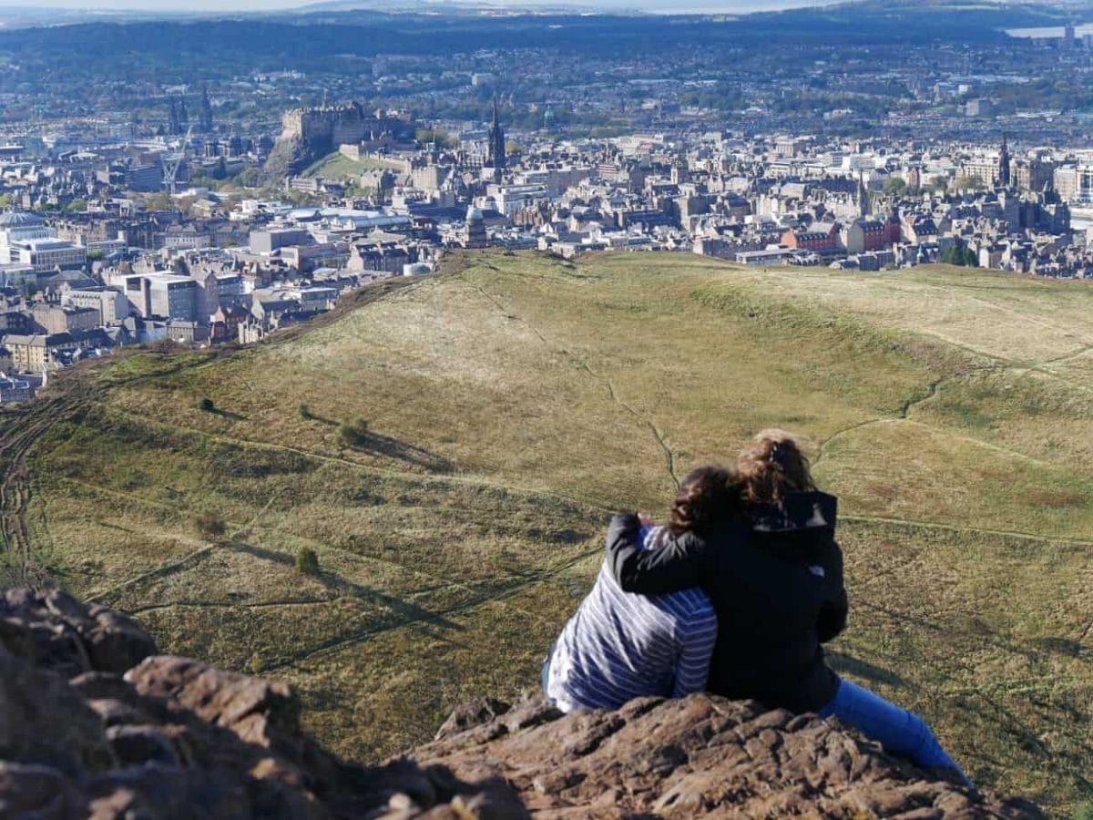 Two girls hugging at the top of Arthur's Seat looking over Edinburgh