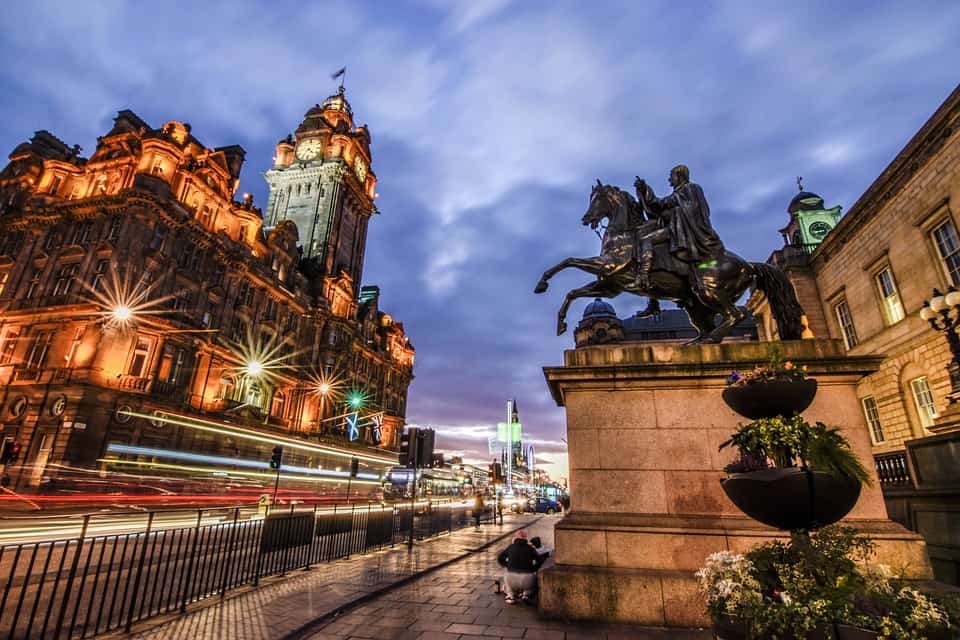 Ediburgh old building with cars driving past at night with statue of man on horse