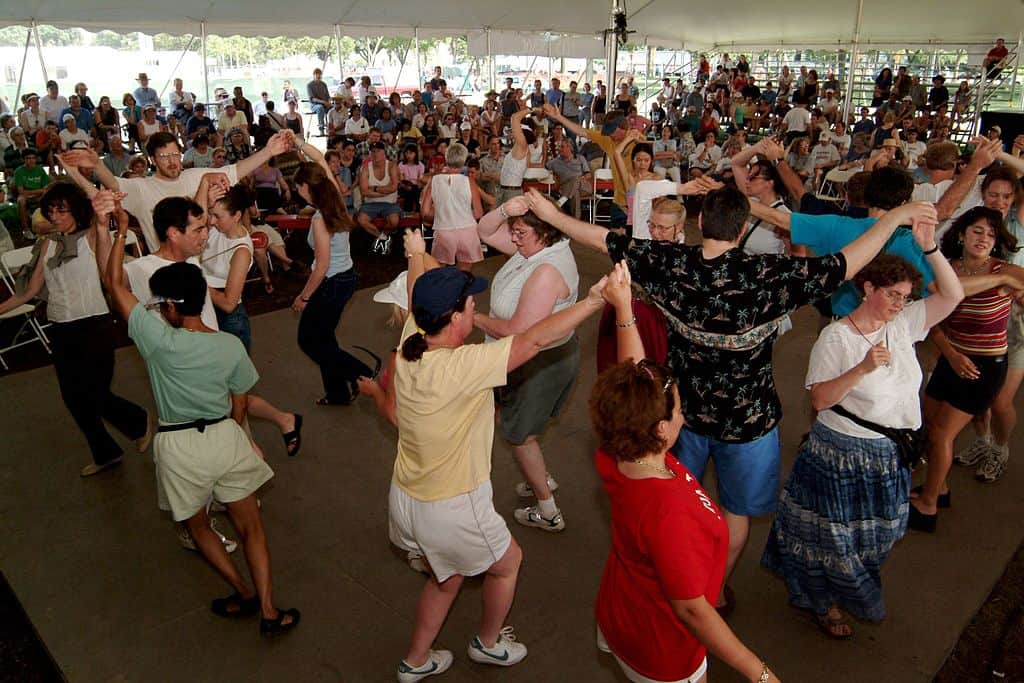 A large number of people doing a Scottish Ceilidh Dance in a tent