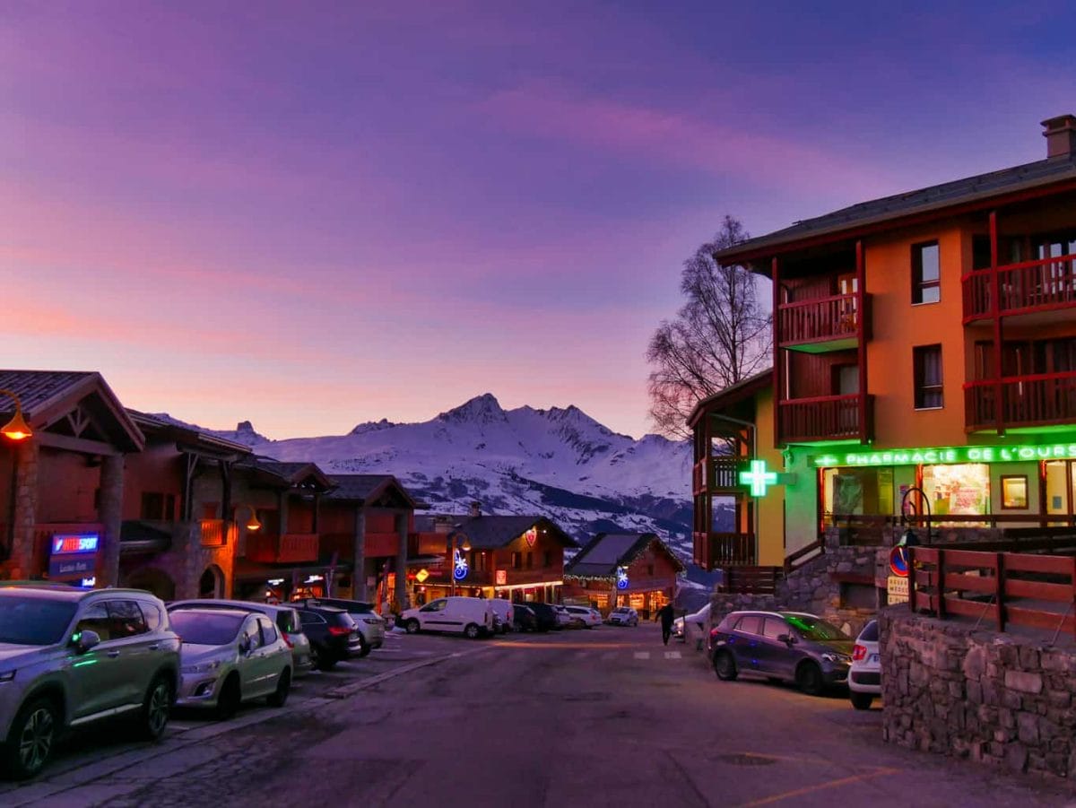 Wooden buildings with shops in Peisey-Vallandry in the evening with a purple and pink sky with snowy mountains in the background