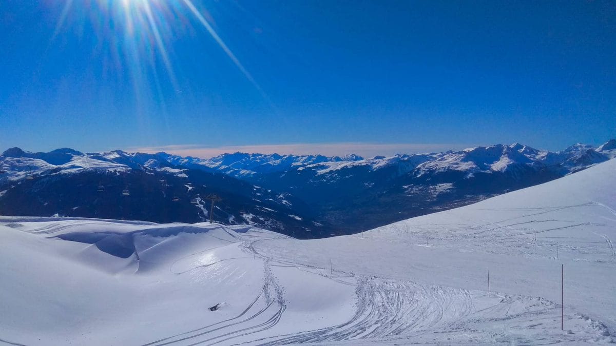 Wide snow covered piste in Les Arcs looking at La Plagne with deep blue sky