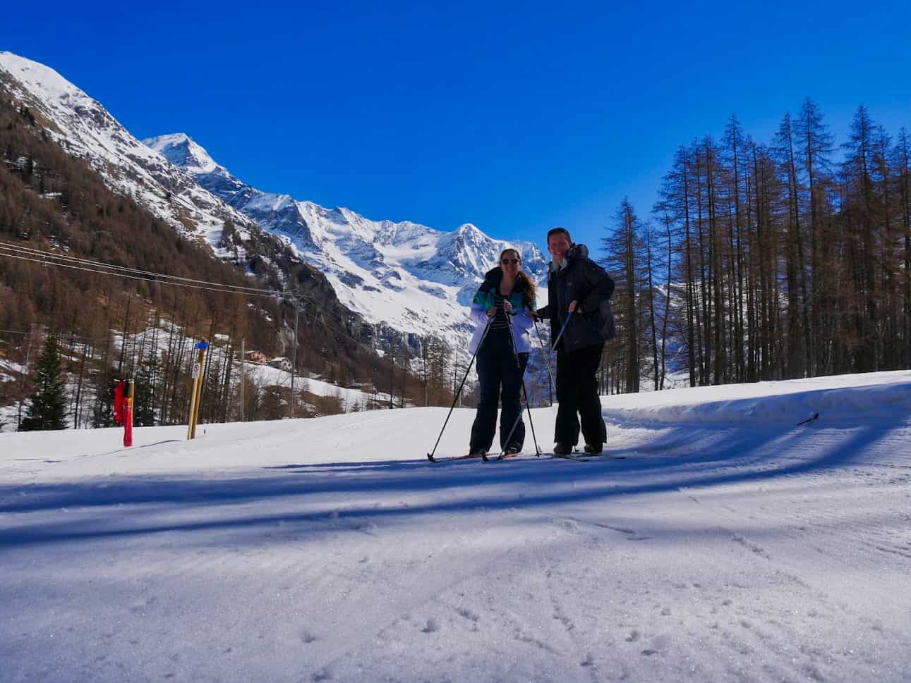 Kalyn and Guy posing with Nordic Skis with snowy mountains in the background