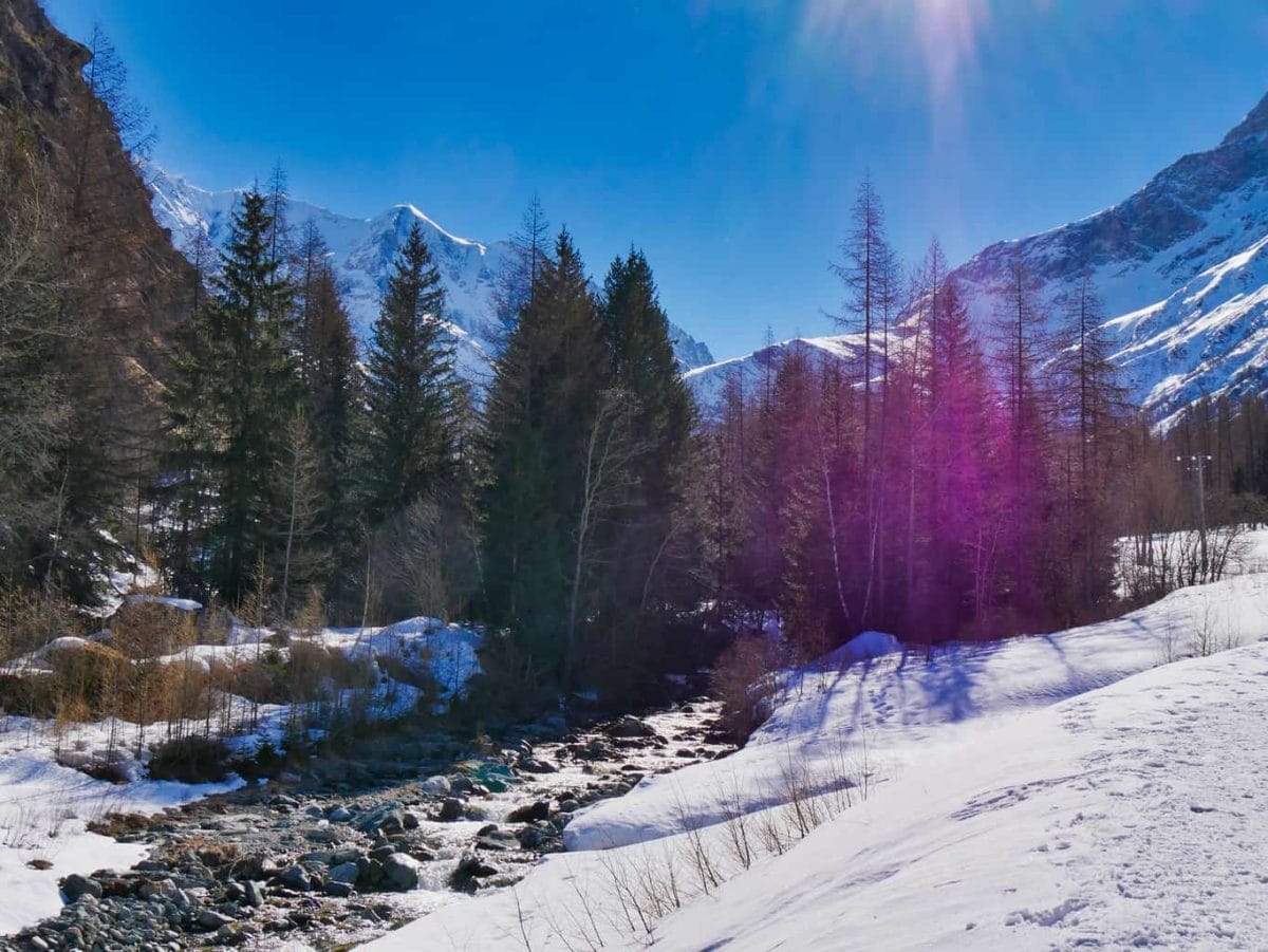 Stream in Nordic Ski Area in French Alps with snow to the side green trees in the background blue sky and snowy mountains