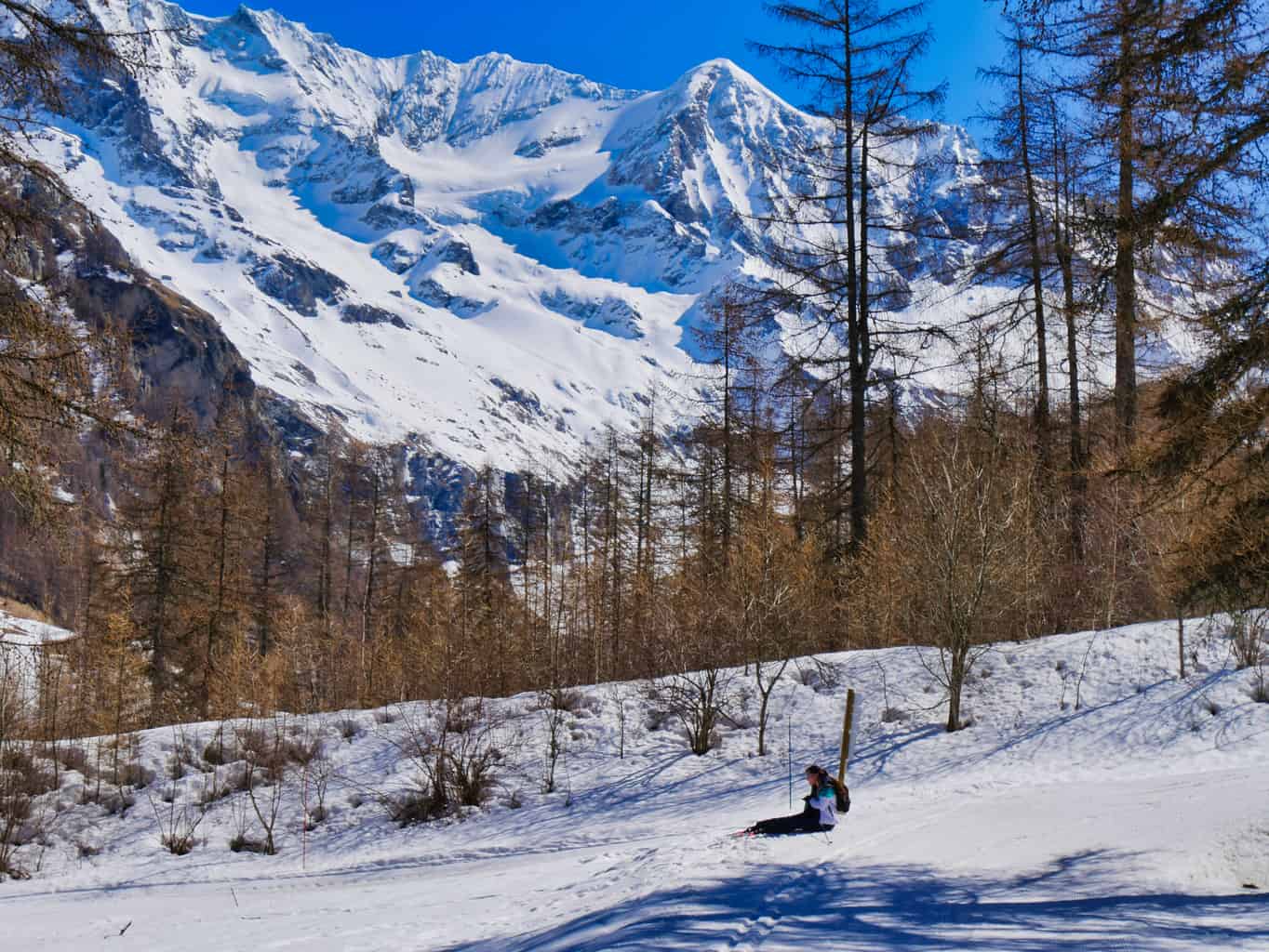 Kalyn on floor struggling to Nordic Ski with snowy mountains in the background