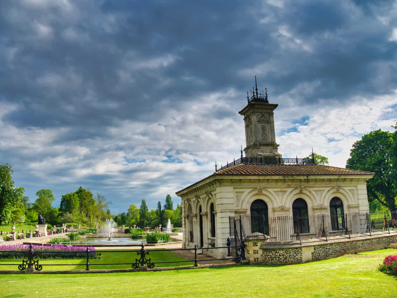 A building in Hyde Park with ominous clouds and water fountains behind