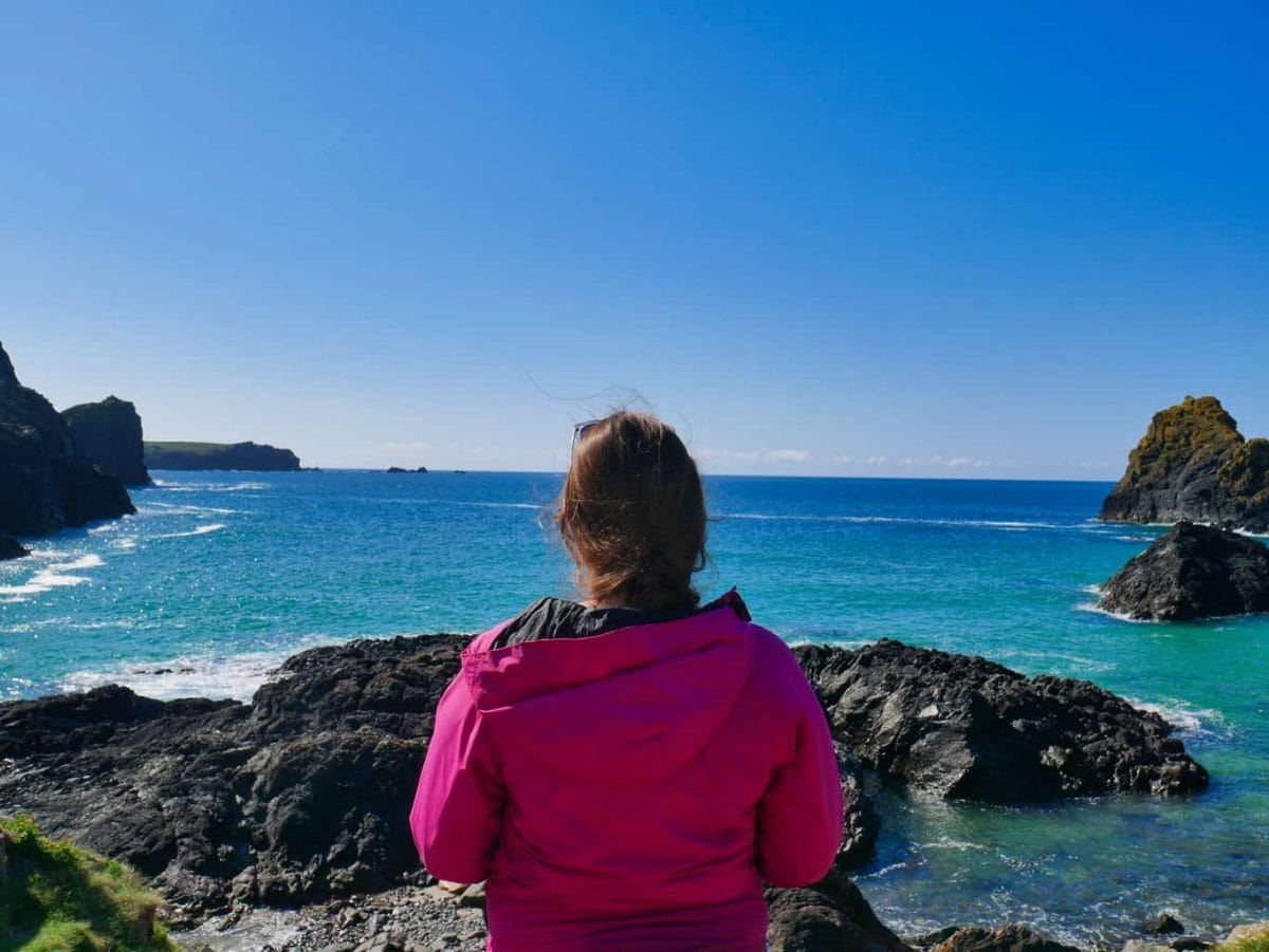Kalyn looking out over the crystal clear blue water of Kynance Cove with deep blue sky