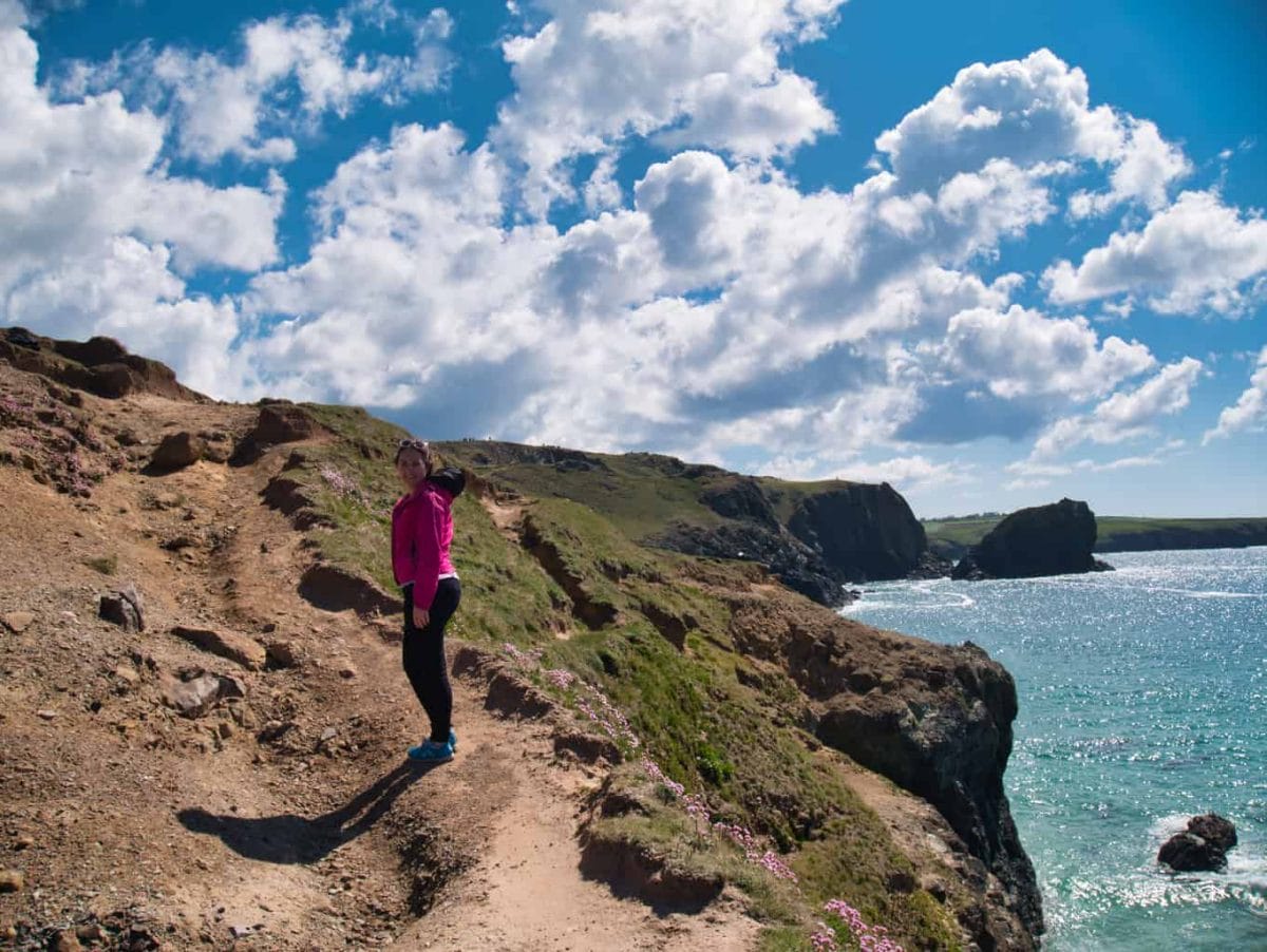 Kalyn walking on the cliffs at Kynance Cove with blue sky and clouds and light blue water in the background