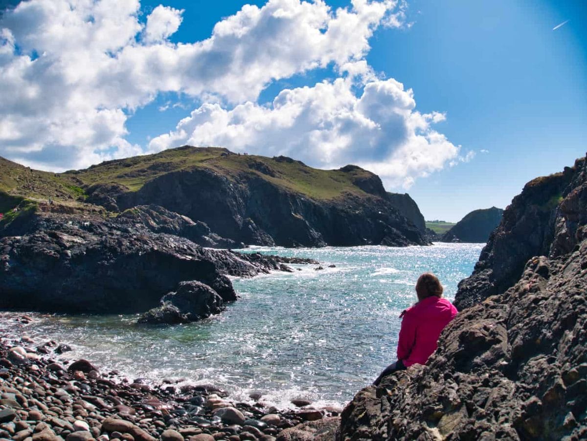 Kalyn sitting on a rock looking out over the blue water at Kynance Cove