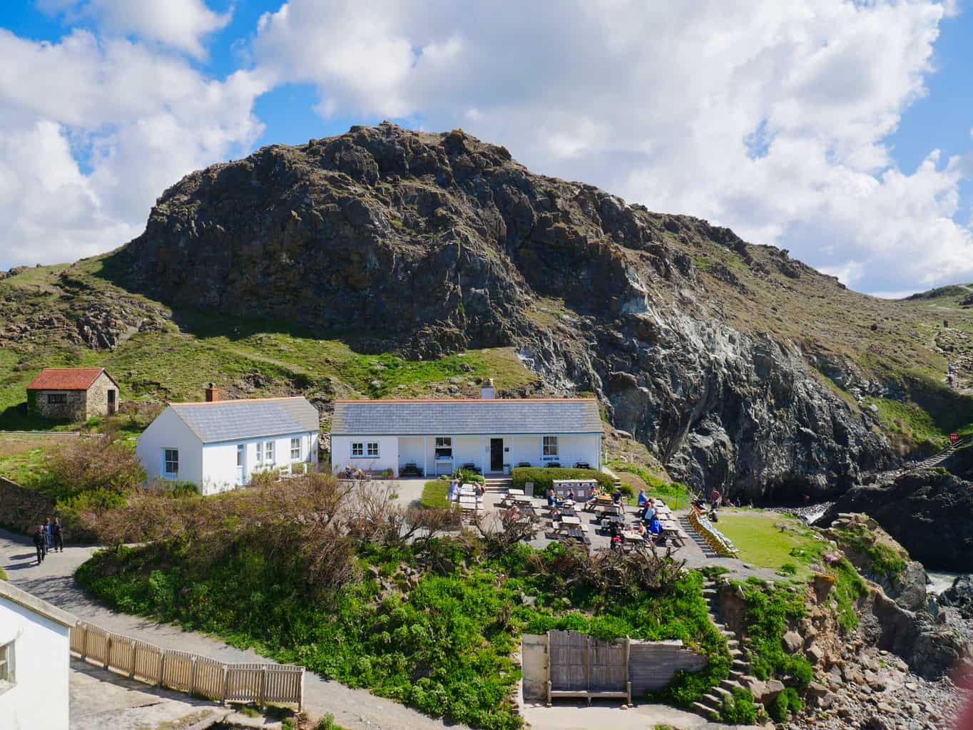 White cafe at Kynance Cove with green grass rock behind and water in front with people at the cafe