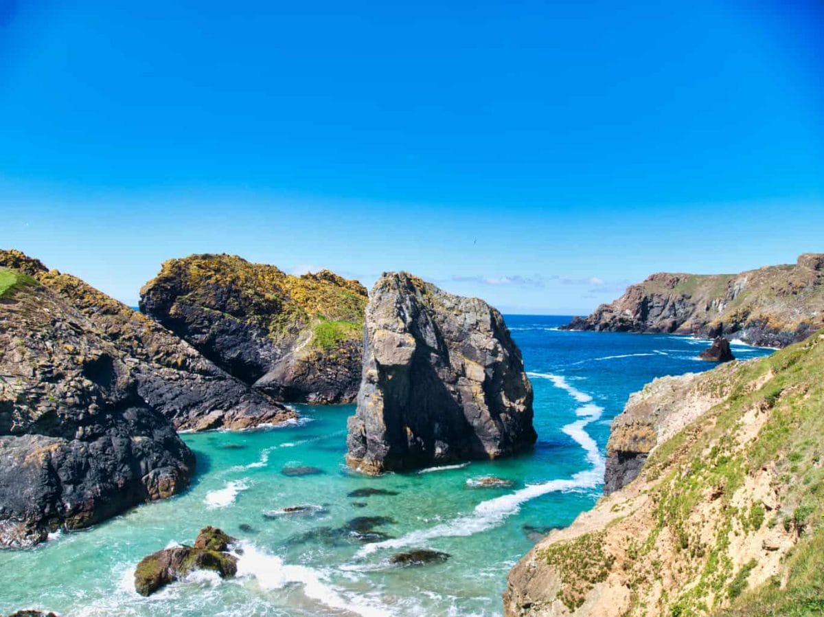 View of Kynance Cover from above with deep blue sky and stunning blue water with rocks sticking out