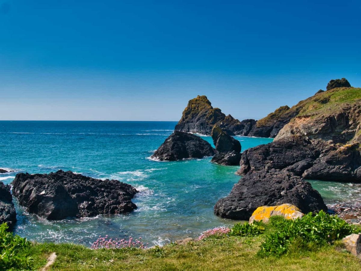 The view form a cliff at Kynance Cove looking over deep blue water with a clear blue sky and rocks coming out of the water