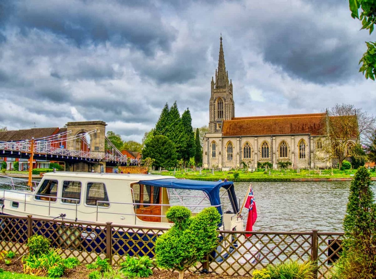 A boat on a river in Marlow with a church behind with dark clouds and green trees