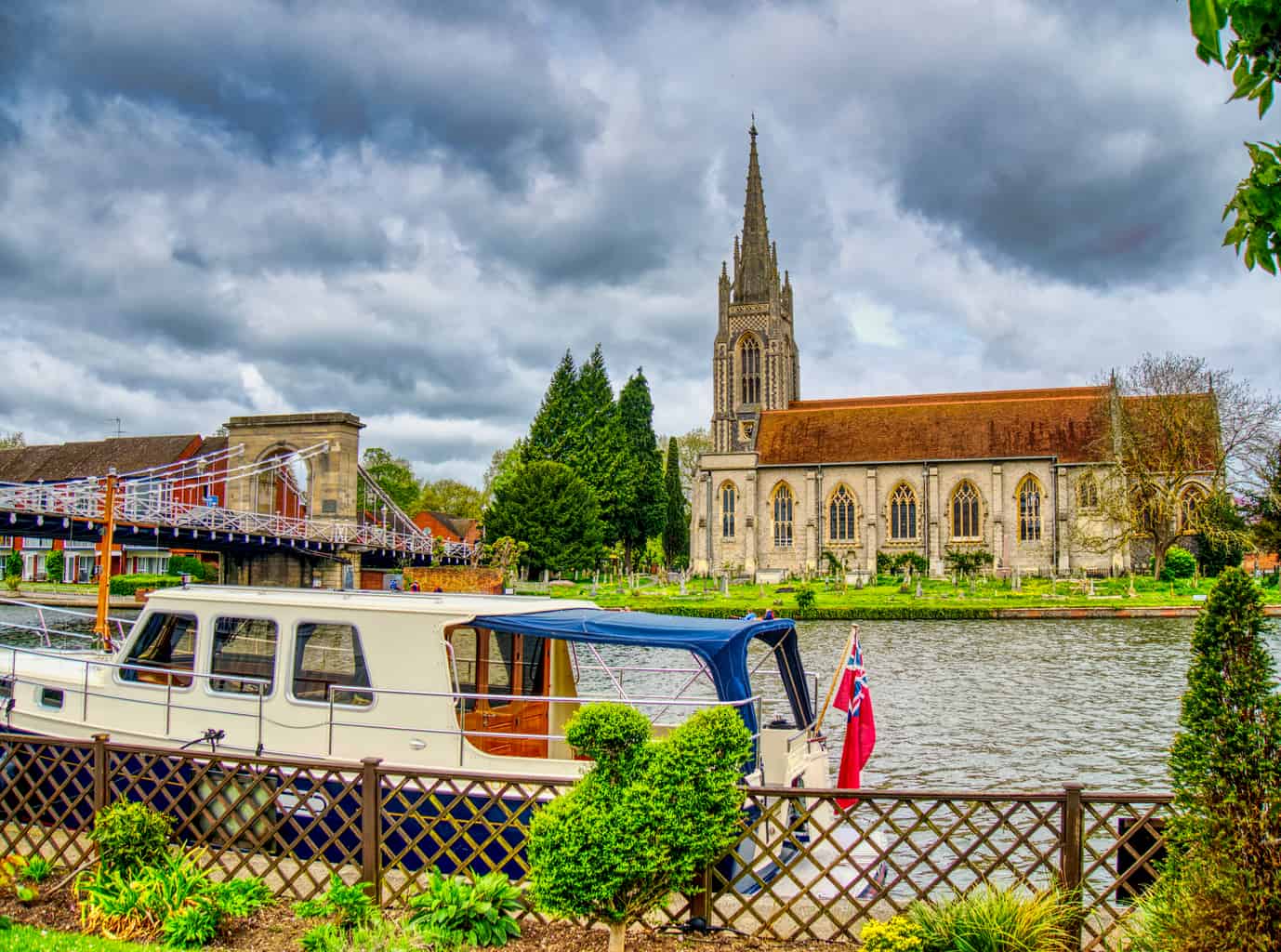 A boat on a river in Marlow with a church behind with dark clouds and green trees