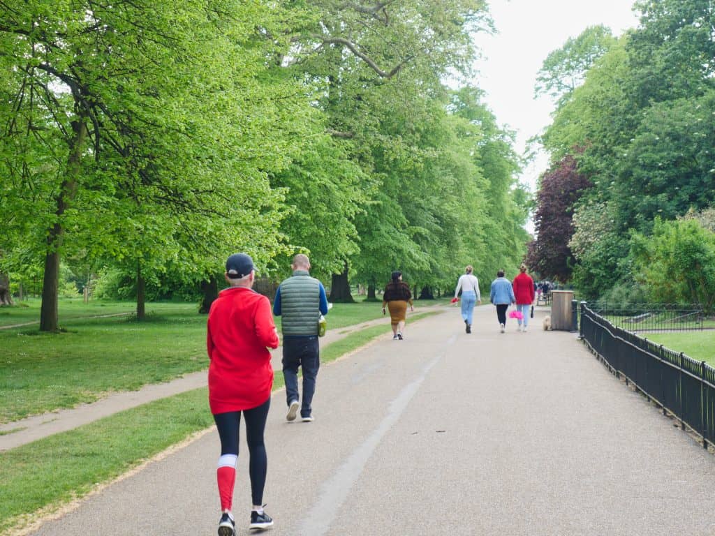 A lady in red running in Hyde Park with walkers in front of her
