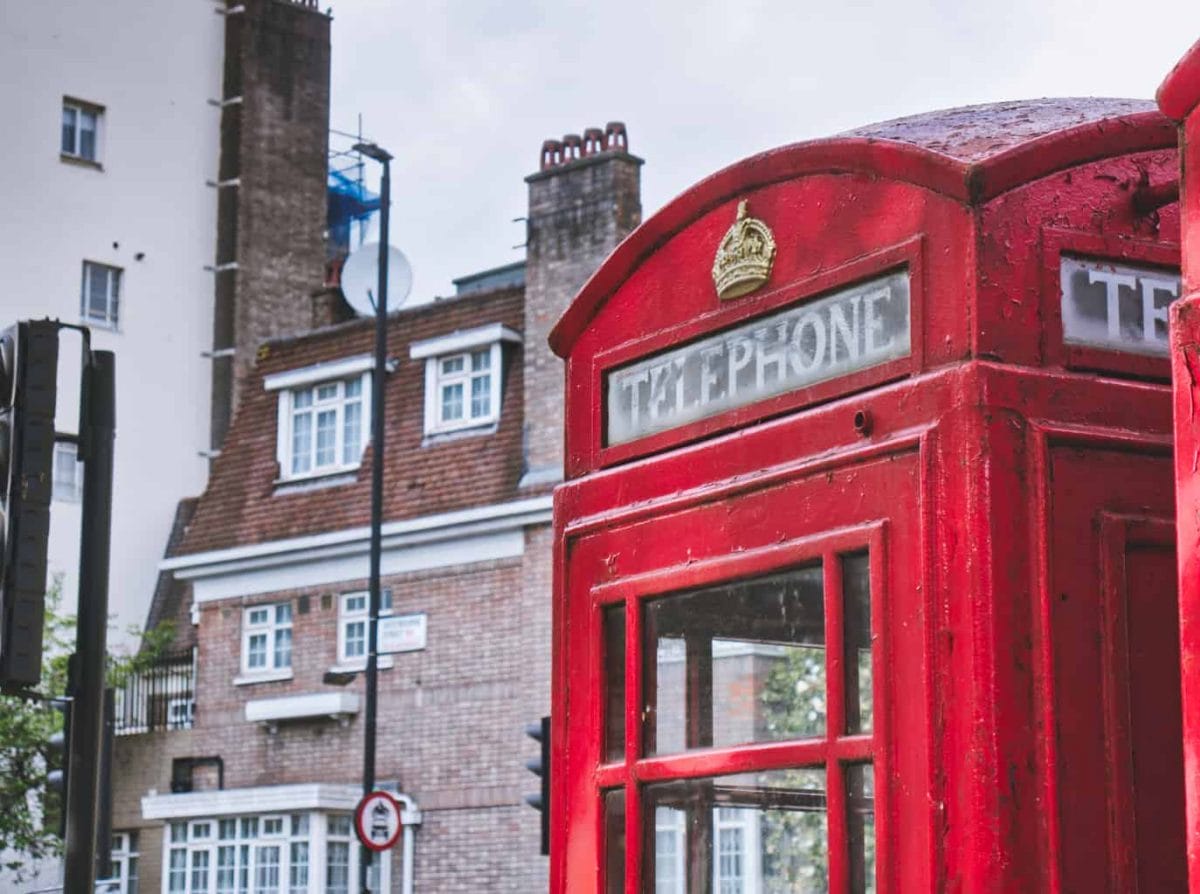 A red telephone booth in London with a building behind with muted colours