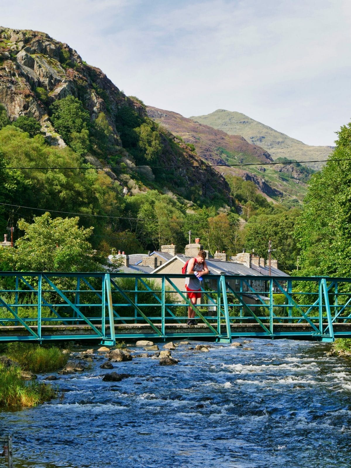 A man on bridge in Beddgelert Wales with a river flowing underneath and hills in the background