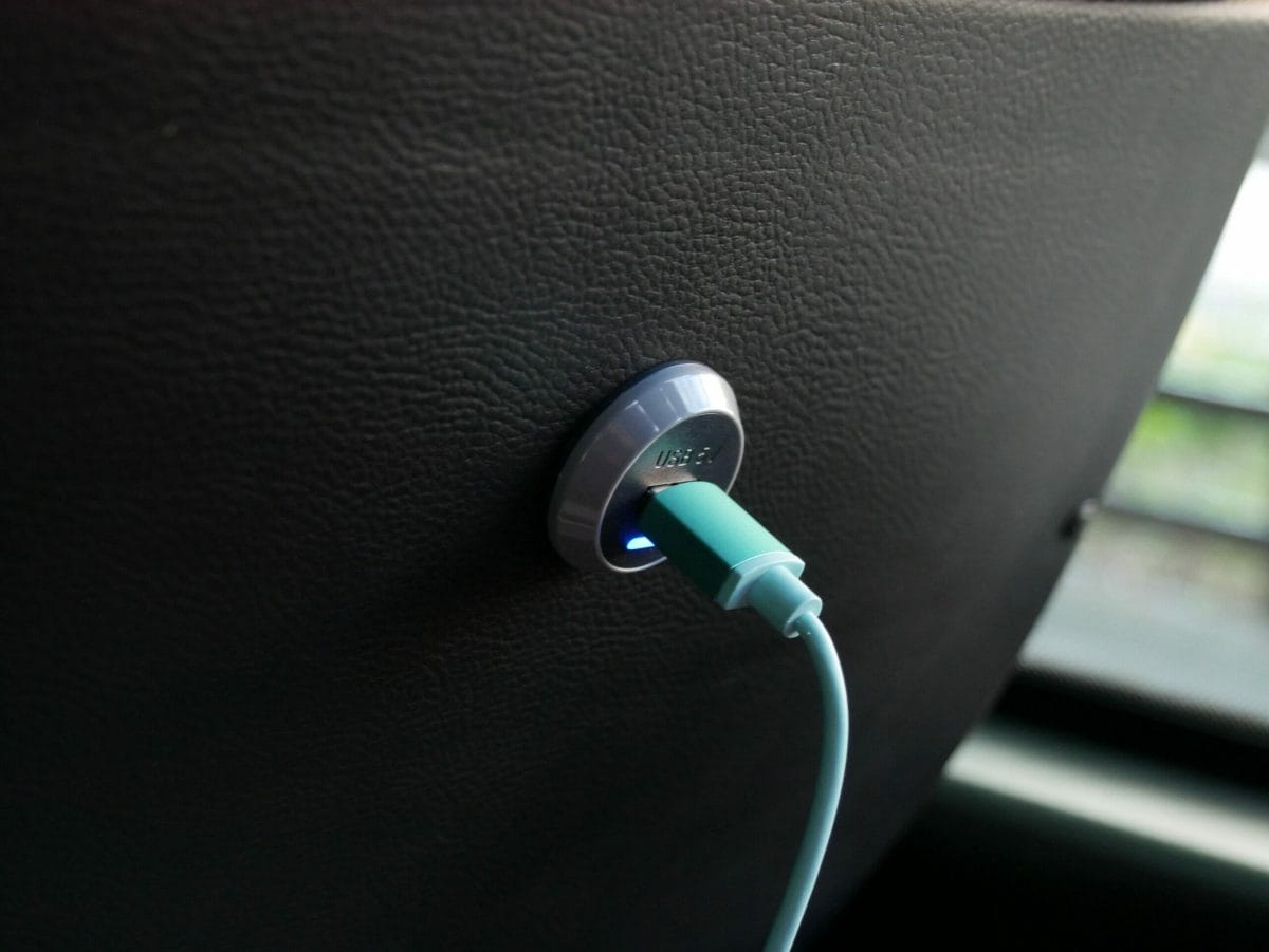 A USB charging point in the back of a seat with a green USB cable plugged in to it