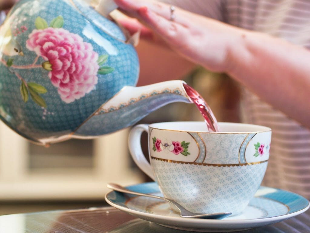 Kalyn pouring red berry tea from a floral tea pot in to a floral mug