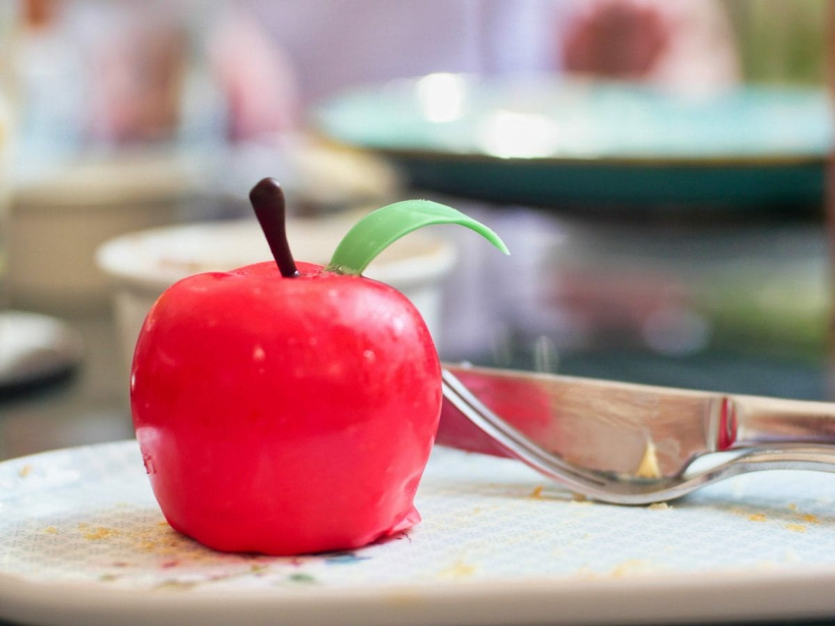 A dessert made to look like a red apple on a plate with a knife and fork