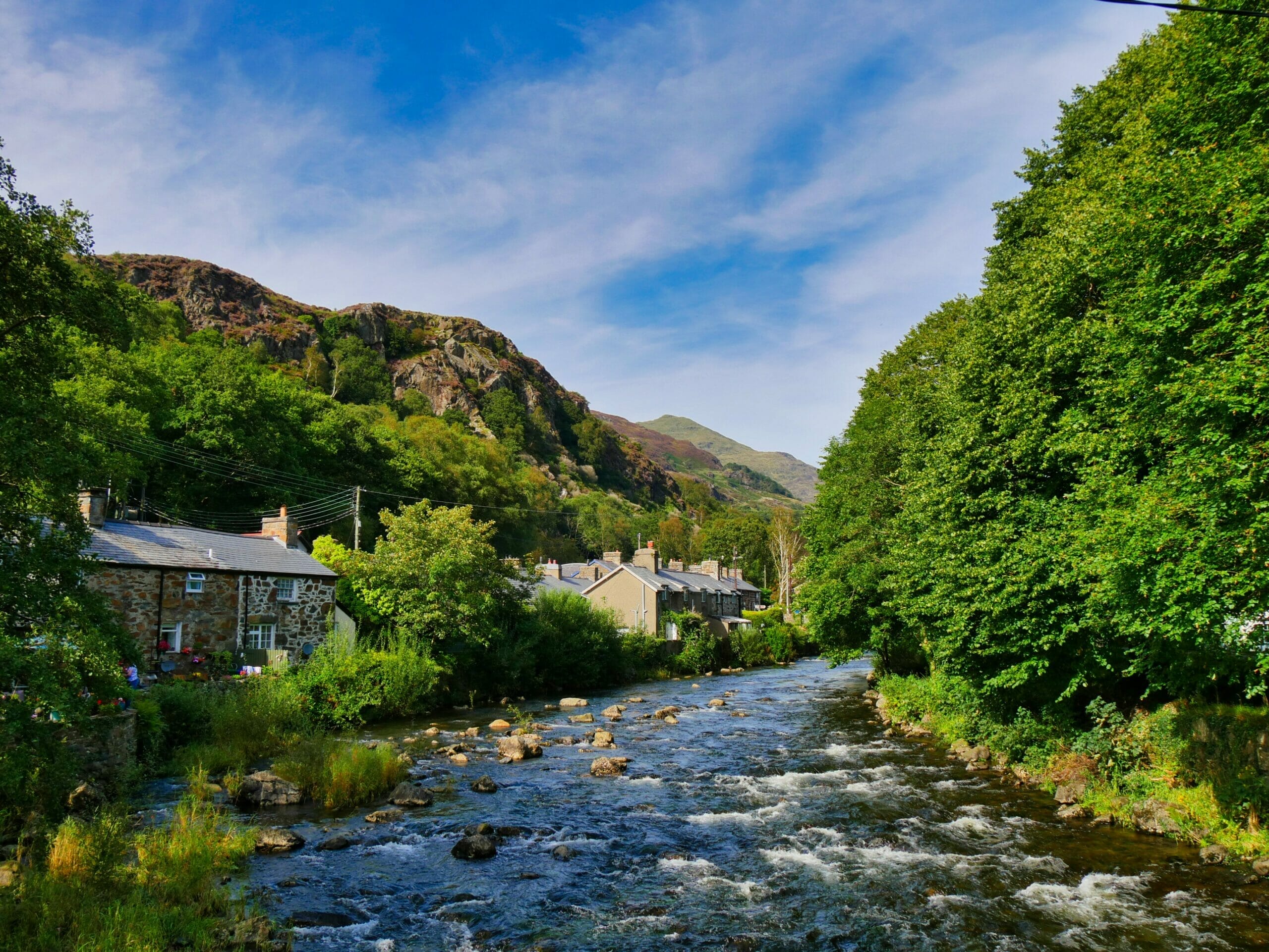 Stone cottages with river running past them and blue sky in Wales