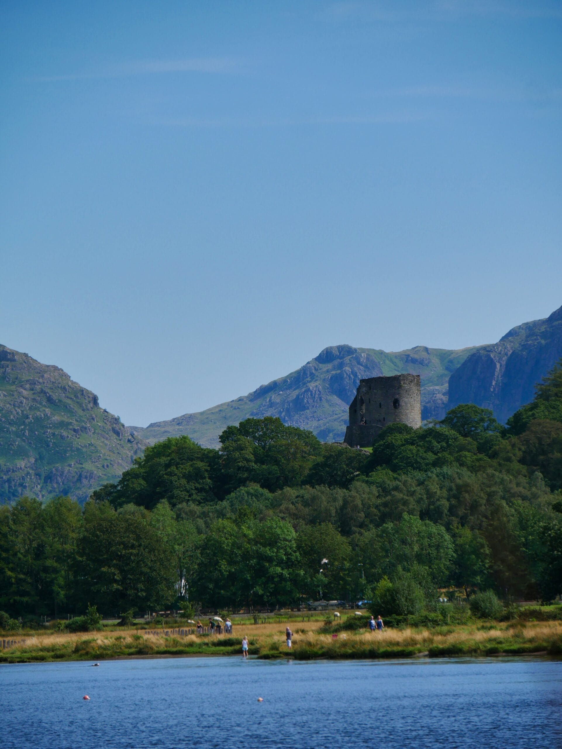 A lake in Wales with a ruined castle in the background and mountains in the deep background