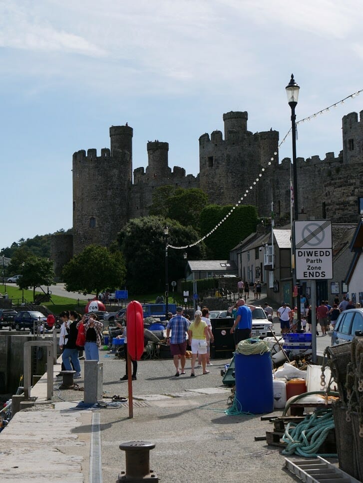 People walking along the street overlooked by the castle in Conwy, North Wales
