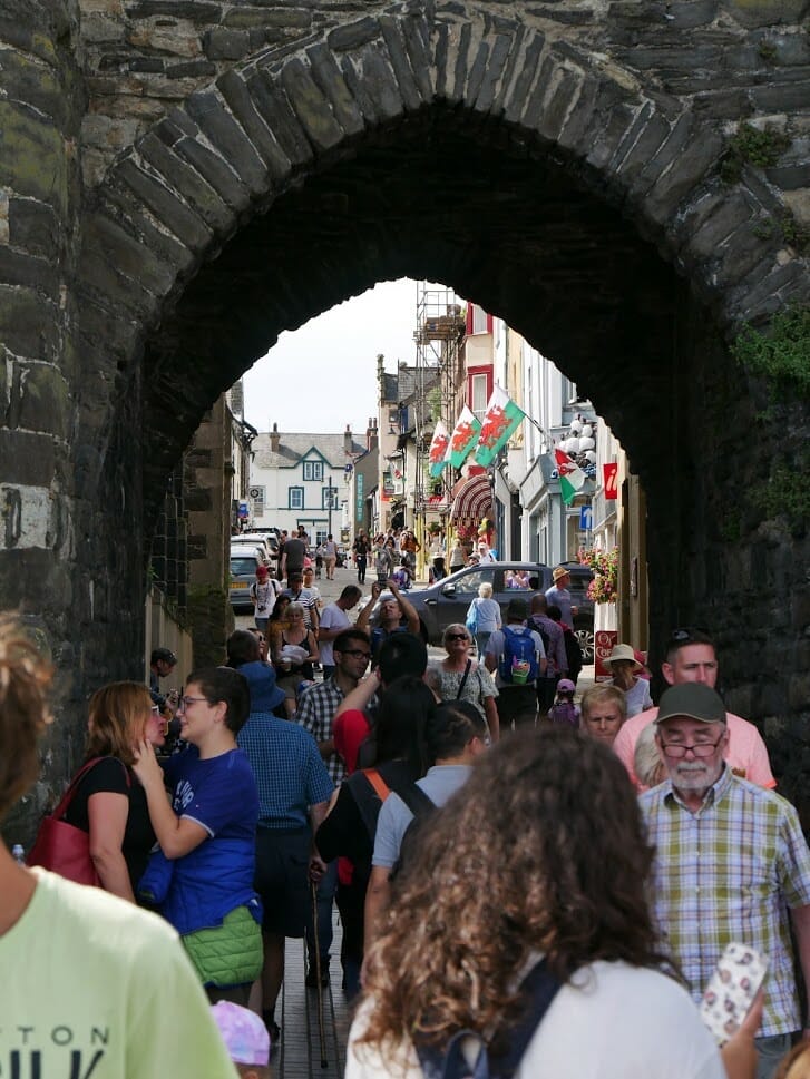 People walking under an old stone arch in Conwy