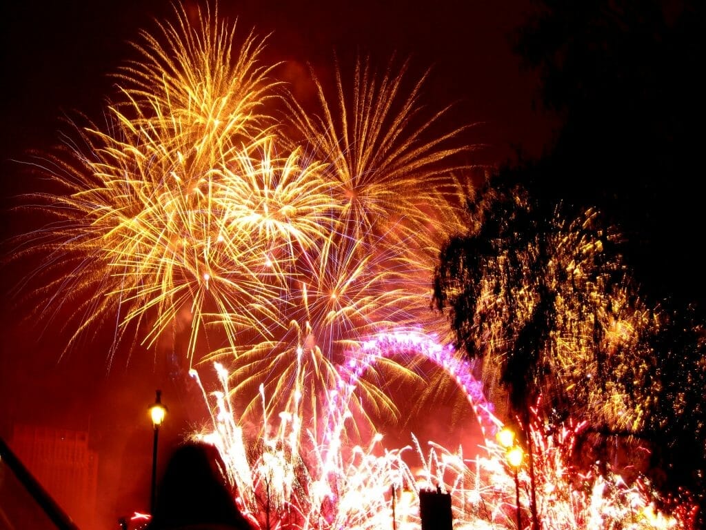 Fireworks going off at the London Eye, with the London Eye lit in purple