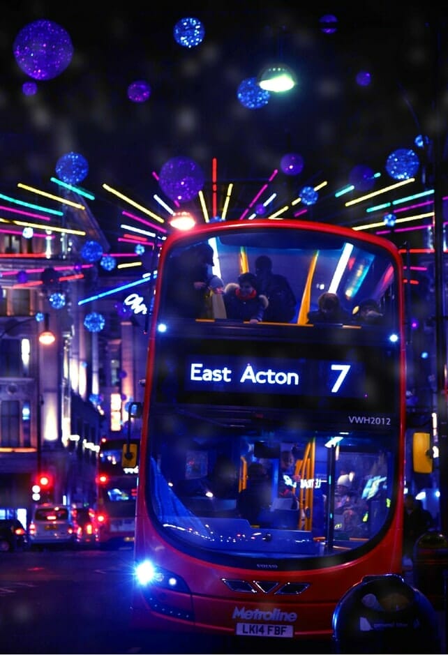 A London bus at night with neon Christmas lights behind