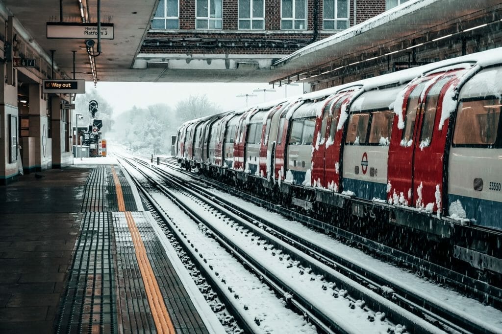 A London underground train with snow on it and snow on the tracks