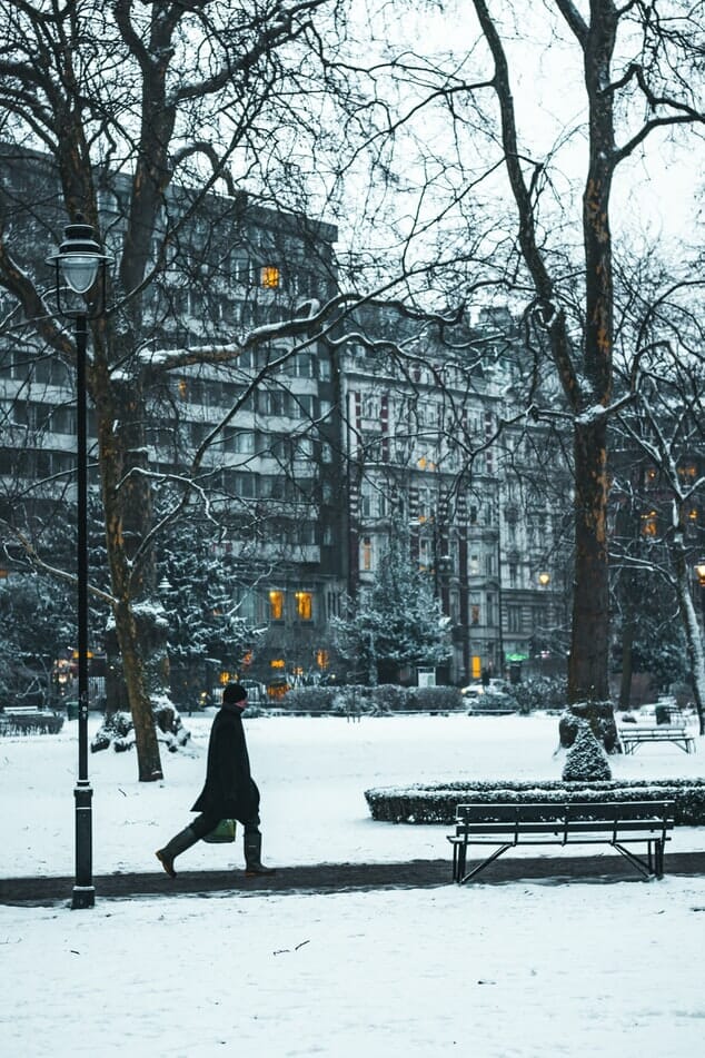 A man walking towards a park bench in a snowy London park