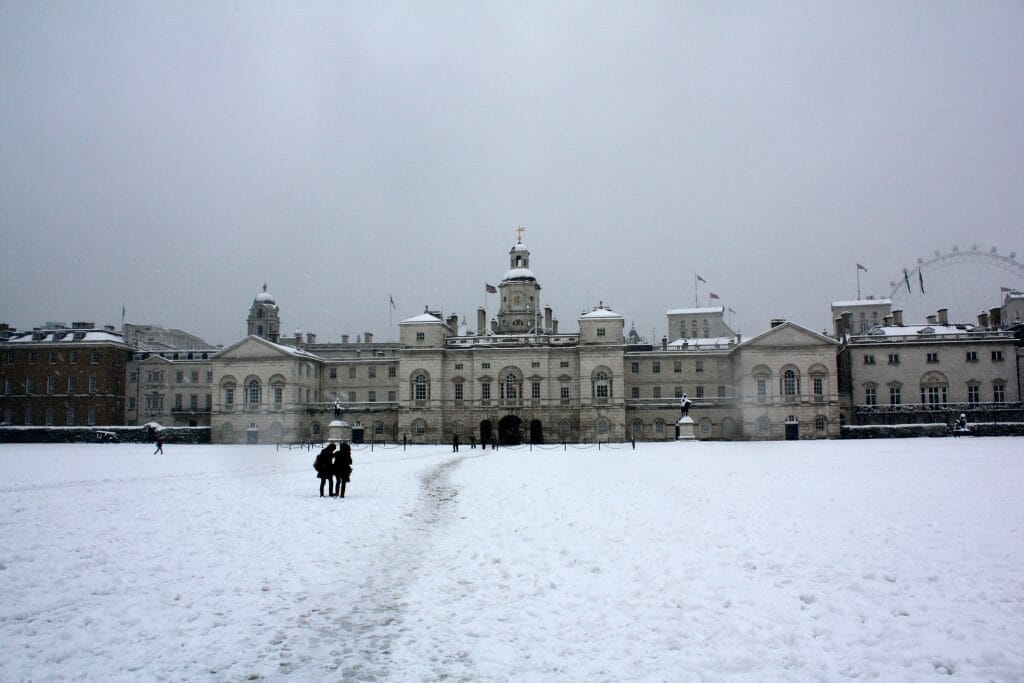 A London Palace with the London Eye in the background with snow on the ground and a grey sky