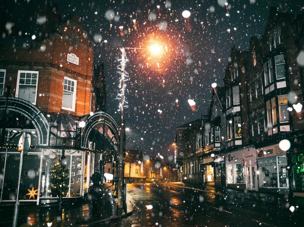 Snow coming down on a London street at night with a lamp in the background