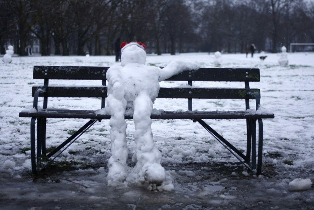 A snowman on a bench with a red hat on in London