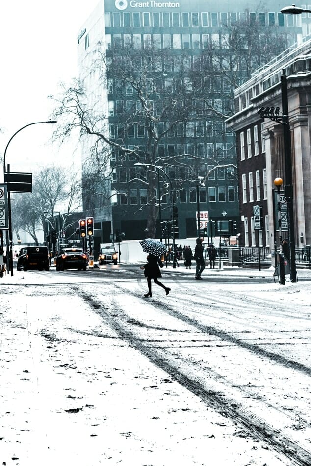 A woman with a black and white polka dot umbrella crossing a snowy road in London